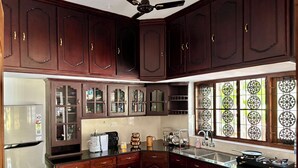 A kitchen with dark wooden cabinets, a stainless steel refrigerator, a built-in oven, and a window with decorative glass panes. - Tranquil 2-Bedroom Haven with AC near Varkala North Cliff (Varkala)