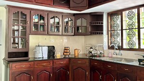 Una cocina con armarios de madera oscura, encimera de mármol, ventilador de techo y ventana con vidrios decorativos.