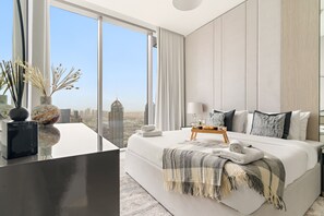 Et moderne soveværelse med en stor seng, et natbord, en lampe og udsigt over bybilledet.