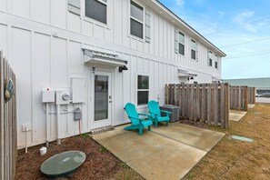 A white two-story house with a wooden deck, two turquoise Adirondack chairs, and a concrete patio.