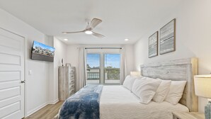 Quarto com cama, ventilador de teto, televisão na parede e janela com cortinas.