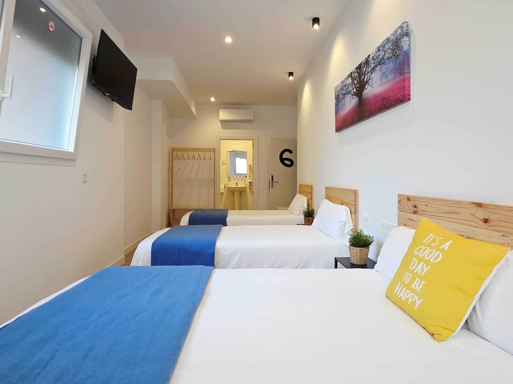 Een hotelkamer met twee bedden, een televisie, een schilderij en een kussen met een motiverende spreuk.