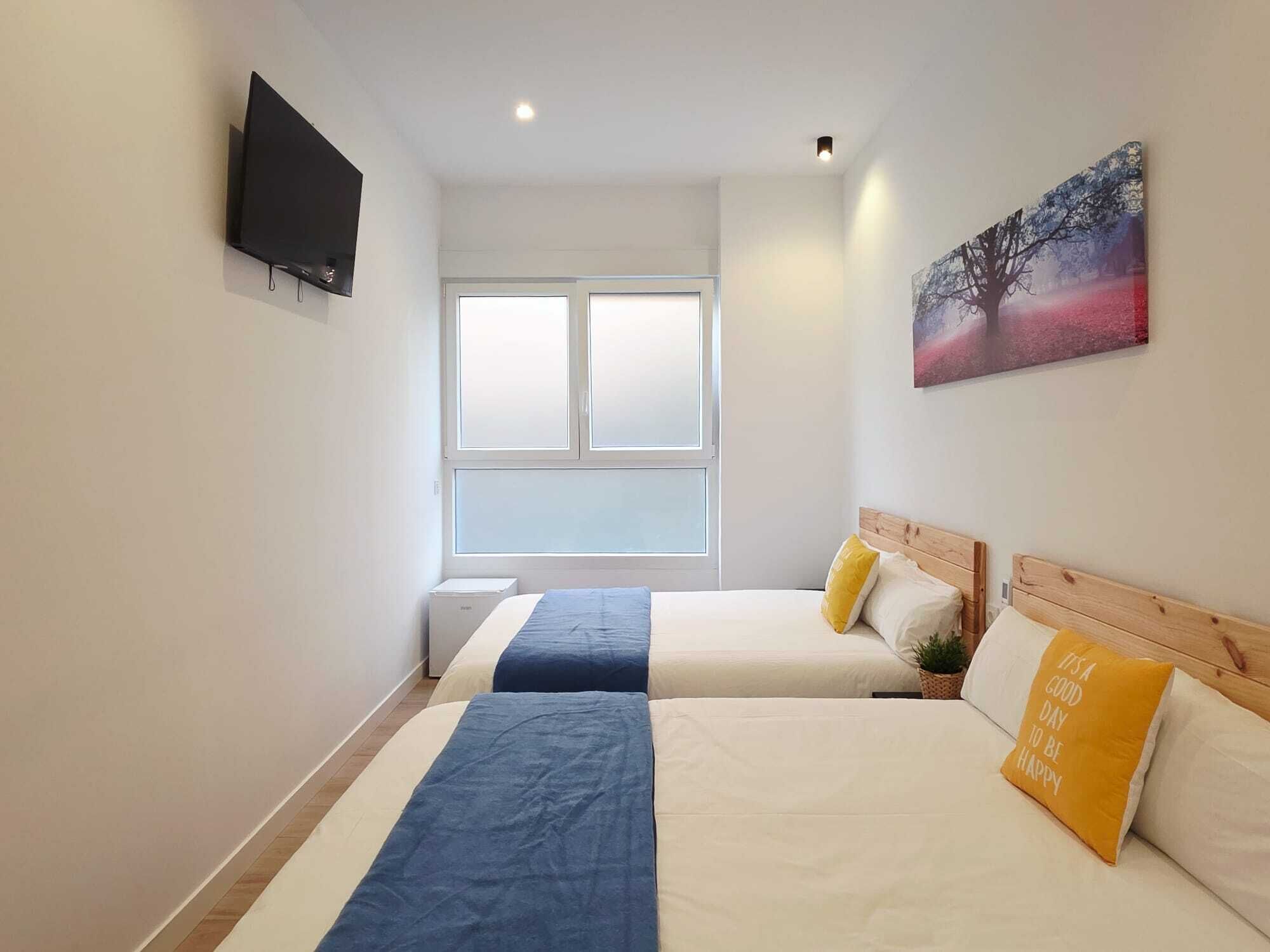Een hotelkamer met twee bedden, een televisie, een raam en een schilderij aan de muur.