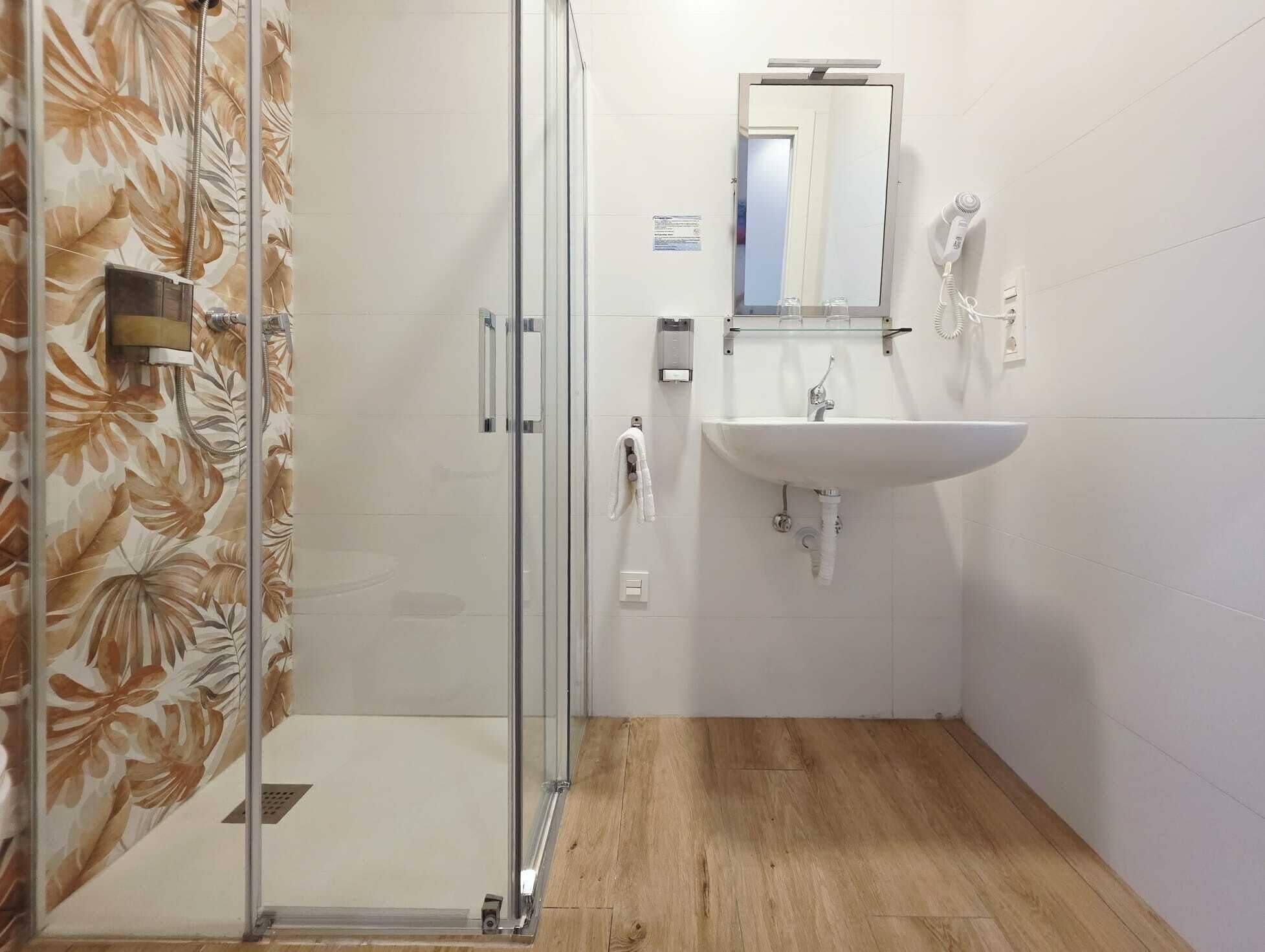 Ein Badezimmer mit Duschkabine aus Glas, Waschbecken mit Spiegel und Handtuchhalter.
