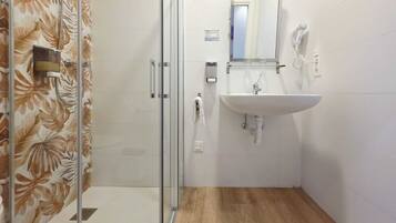 Ein Badezimmer mit Duschkabine aus Glas, Waschbecken mit Spiegel und Handtuchhalter.