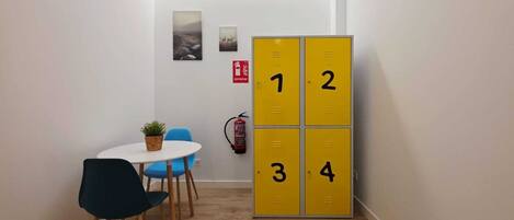 A narrow hallway with a small table and chairs, a yellow locker with numbers, and a fire extinguisher on the wall.