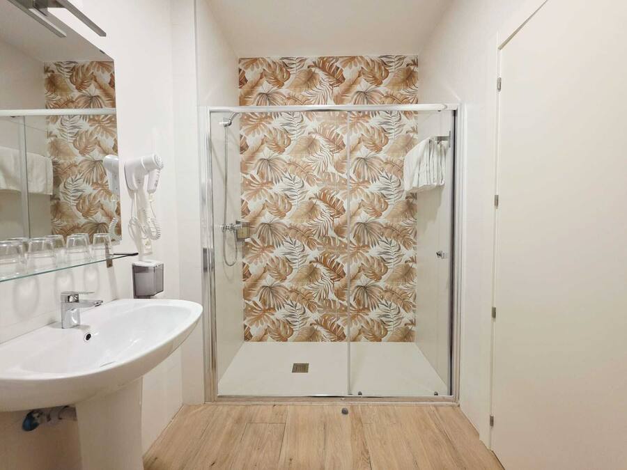 Un baño con cabina de ducha de vidrio, lavamanos y espejo.