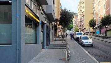 A street view with a building labeled 'ROCKS BIKES' on the left, a sidewalk, parked cars, and a pedestrian walking.