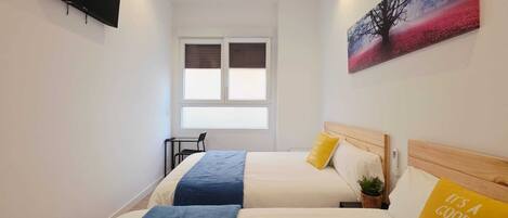 A hotel room with two beds, a TV, a window, and a painting.