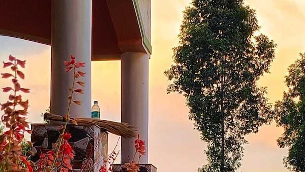 A covered outdoor area with a column structure, surrounded by flowering plants and a tree. - Infinity Viewpoint Homestay (Kalimpong)
