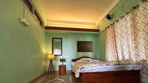 A bedroom with a wooden bed, a bedside table with a lamp, a small plant, and a framed picture on the wall. - Infinity Viewpoint Homestay (Kalimpong)