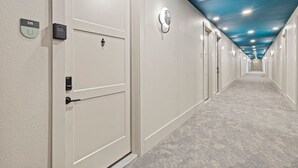 Un couloir d’hôtel avec des portes blanches, des panneaux indiquant le numéro des chambres et un plafond bleu.