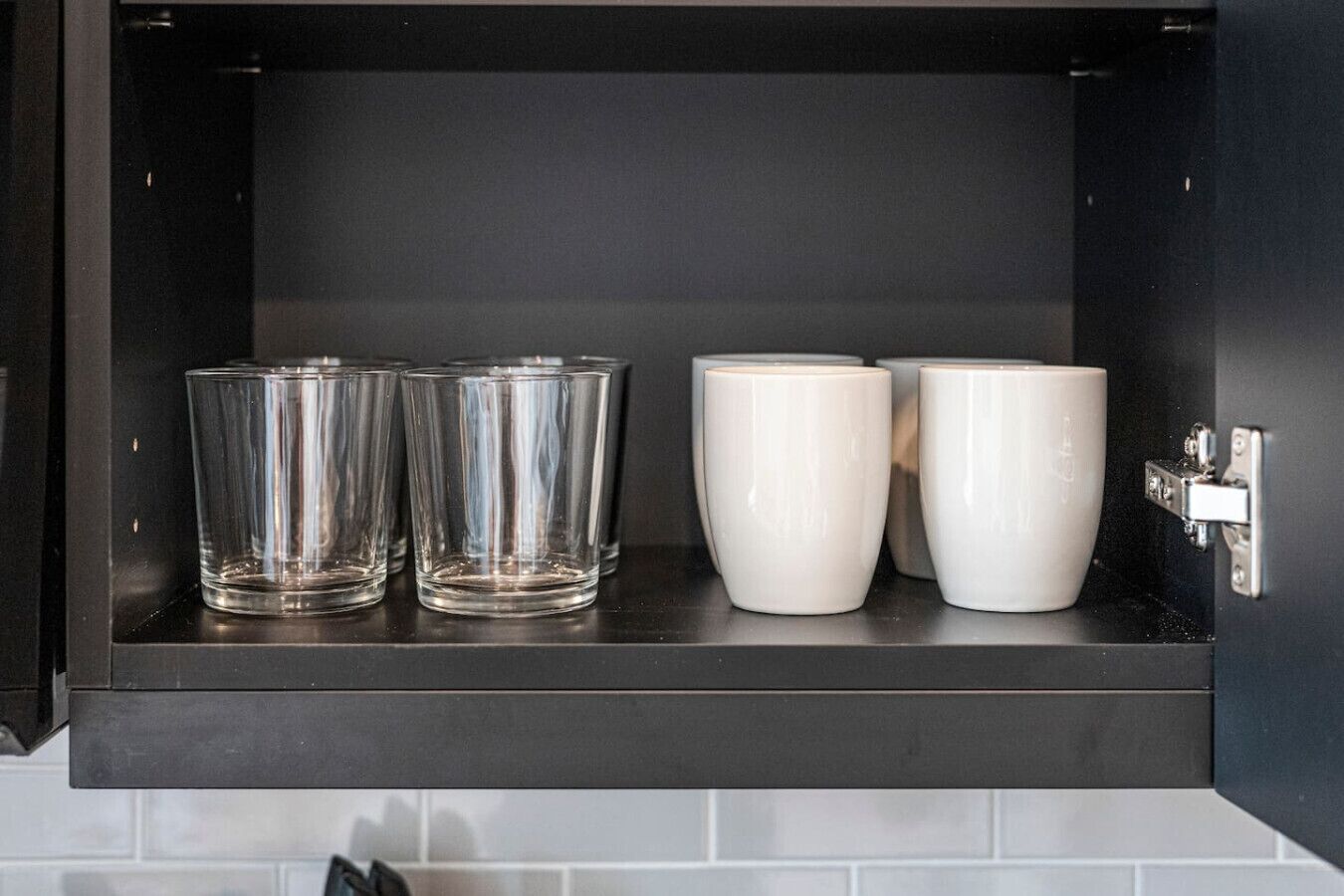 A kitchen cabinet with four glasses and two white mugs.