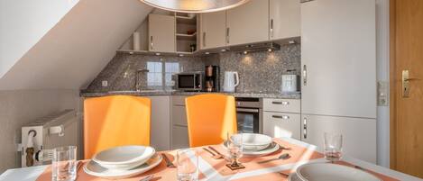 A dining area with a table set for four, equipped with plates, glasses, cutlery, and a yellow pendant light.