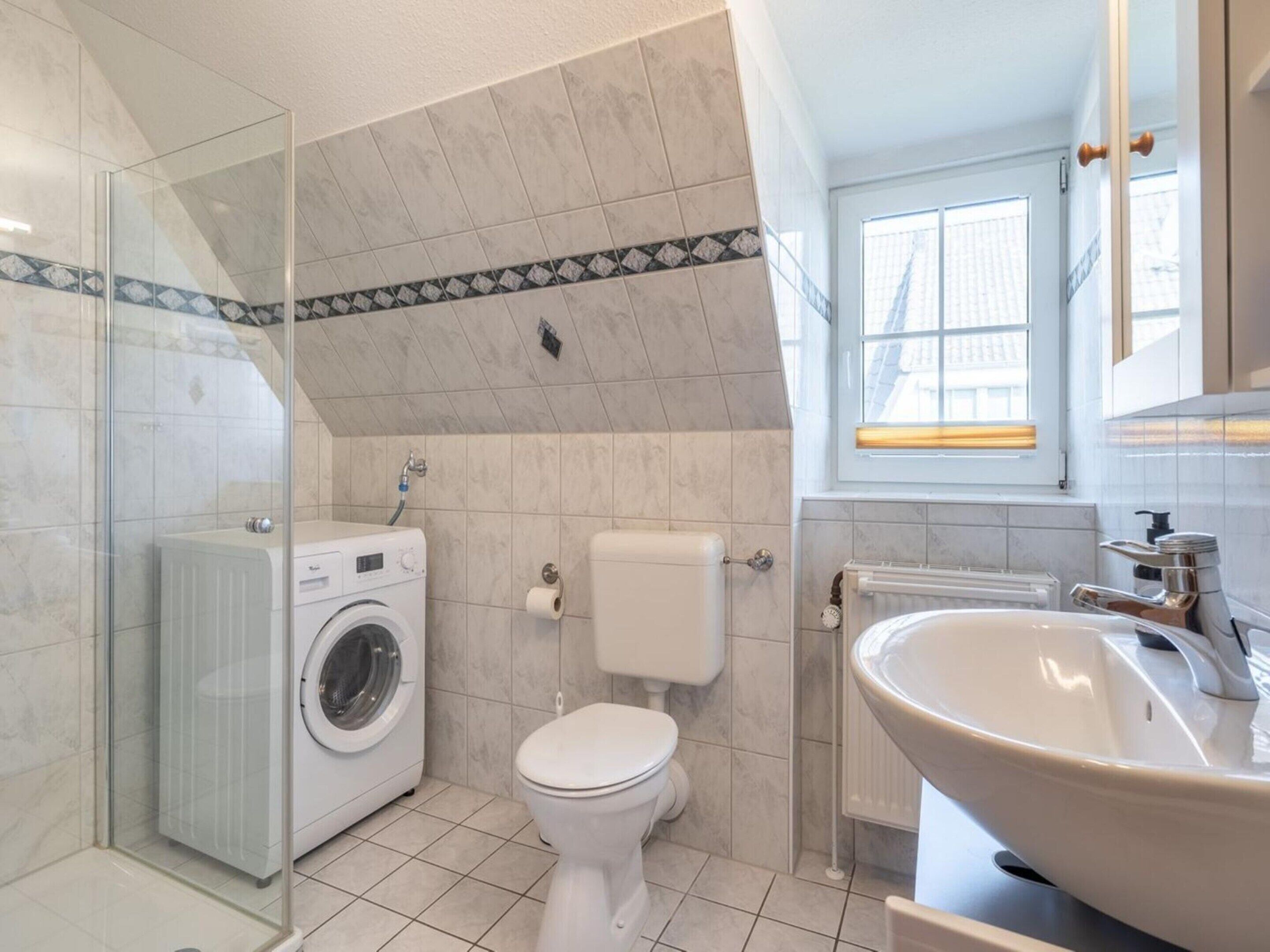 Et badeværelse med brusekabine i glas, vaskemaskine, toilet og håndvask med spejl.