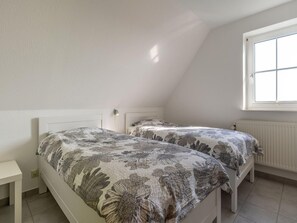 A bedroom with two beds, a bedside table, a window, and a radiator. - Ferienwohnung in Westerdeichstrich (Westerdeichstrich)