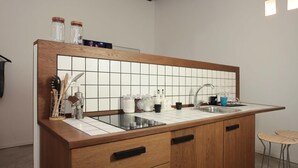 Een keuken met een houten aanrechtblad, een betegelde spatwand en een inbouwgootsteen. Er staan twee krukken bij een klein barretje.