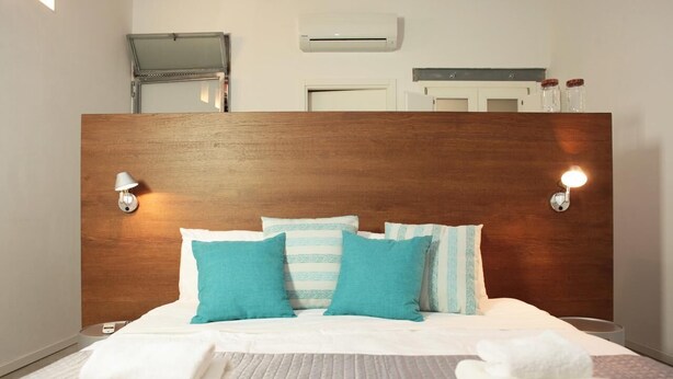 Een keurig opgemaakt bed met witte lakens en teal-kleurige kussens, een houten hoofdbord en twee wandlampen voor het lezen.