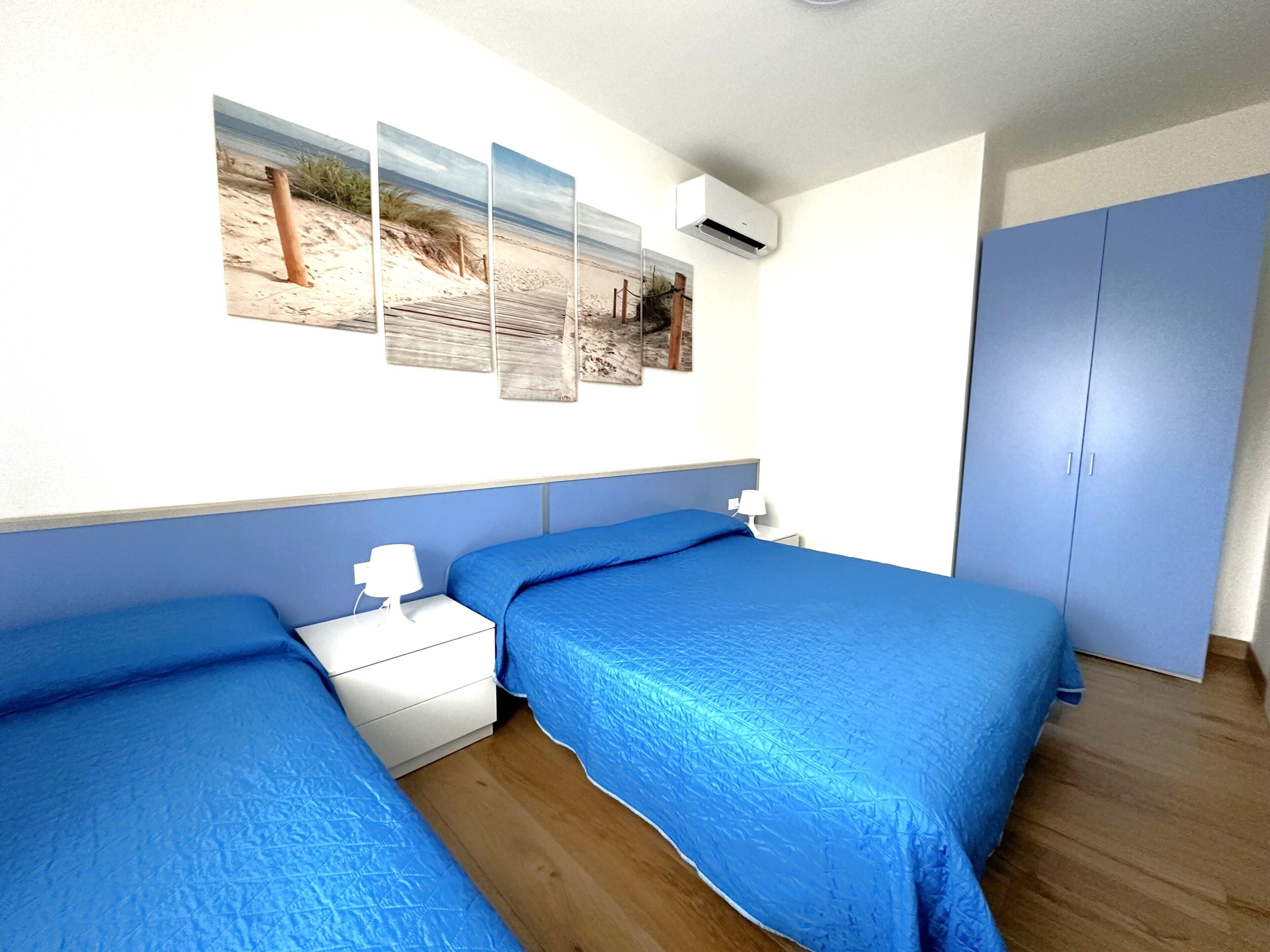 A bedroom with two beds, a nightstand, a wall-mounted air conditioner, and a wardrobe.