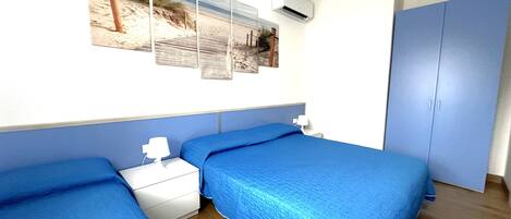 A bedroom with two beds, a nightstand, a wall-mounted air conditioner, and a wardrobe.