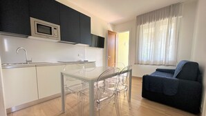 Um espaço de estar compacto com cozinha compacta, área de refeições com mesa e cadeiras, sofá azul escuro e janela com cortinas translúcidas.