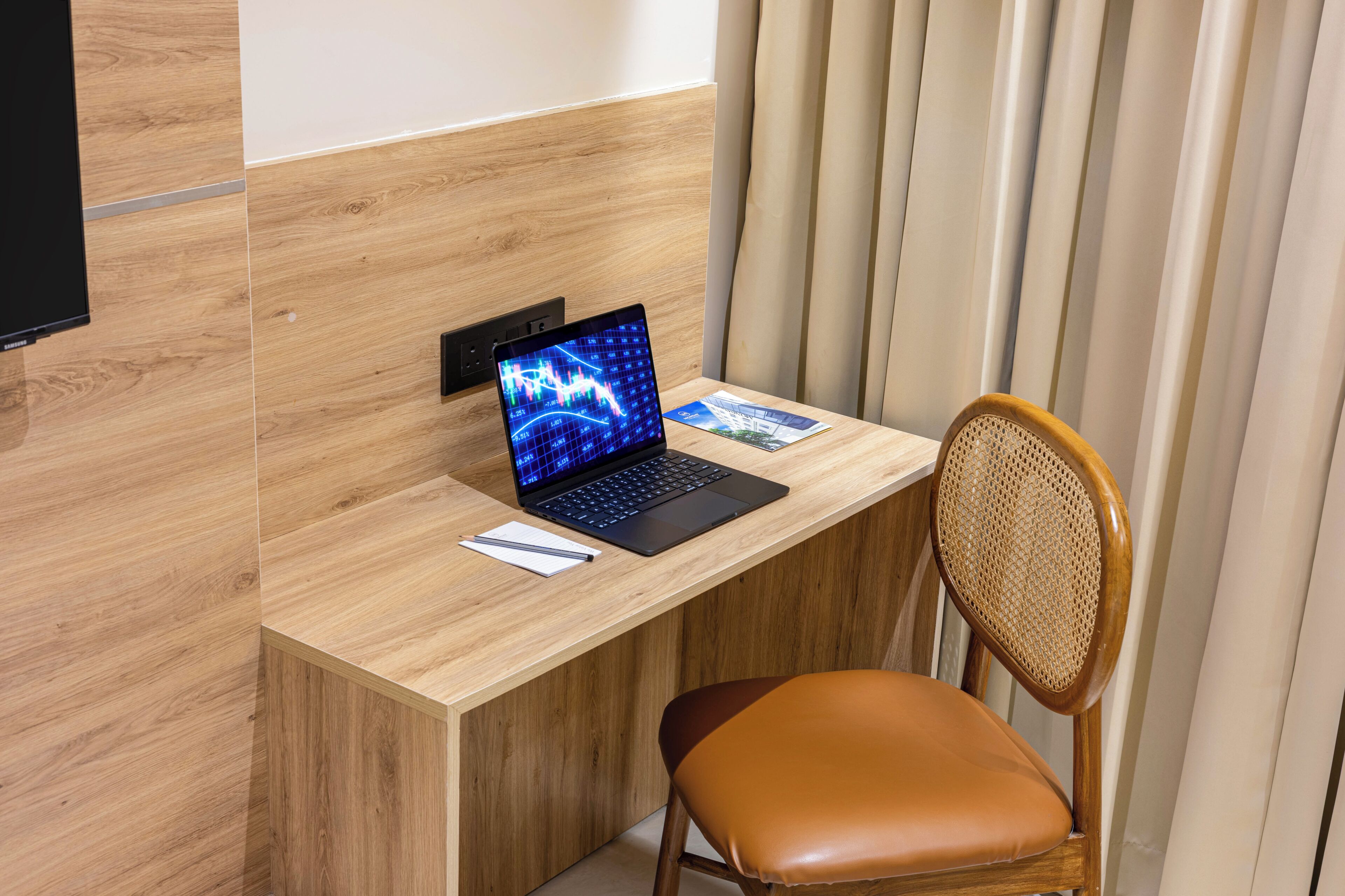 Un bureau en bois avec un ordinateur portable, une chaise et un téléviseur fixé au mur.