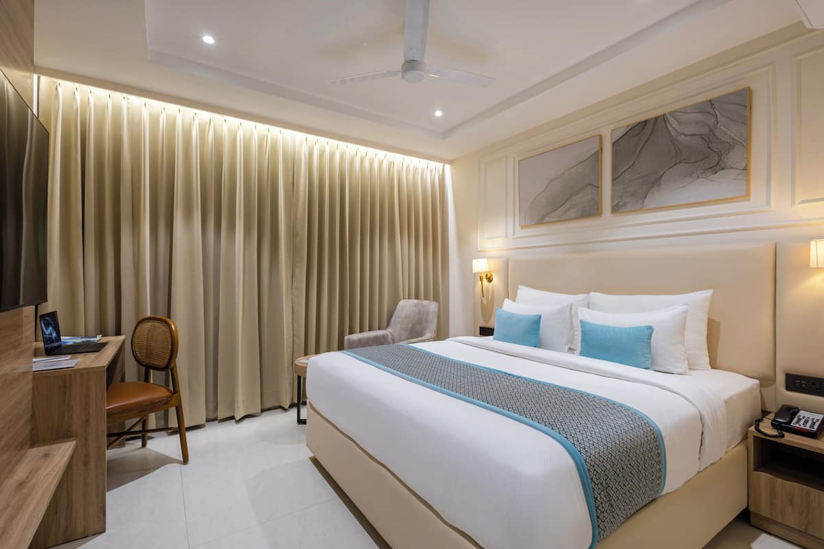 A hotel room with a large bed, a desk, a chair, a desk lamp, and a telephone.