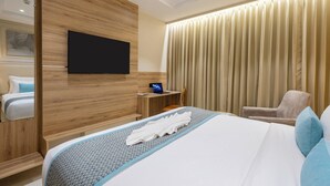 Ein Hotelzimmer mit Bett, Fernseher, Schreibtisch, Stuhl und einem großen Fenster mit Vorhängen.
