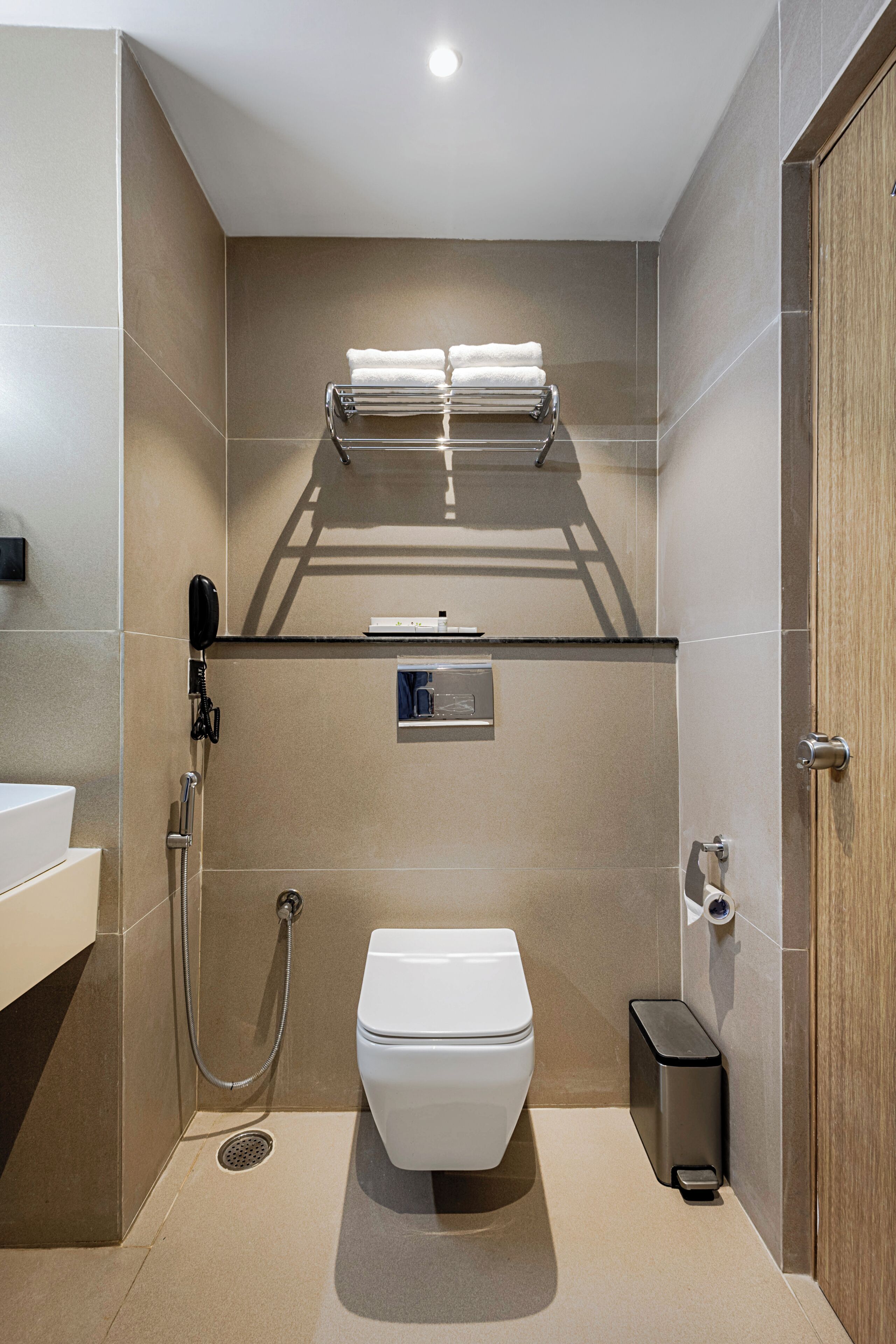 A modern bathroom with a toilet, a shower, a towel rack, and a trash bin.