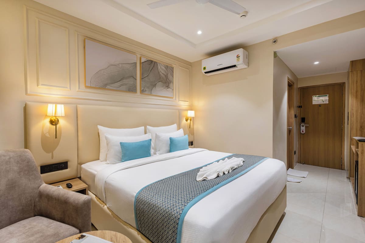 A hotel room with a bed, bedside lamps, an air conditioning unit, a wooden door, and a wall-mounted artwork.