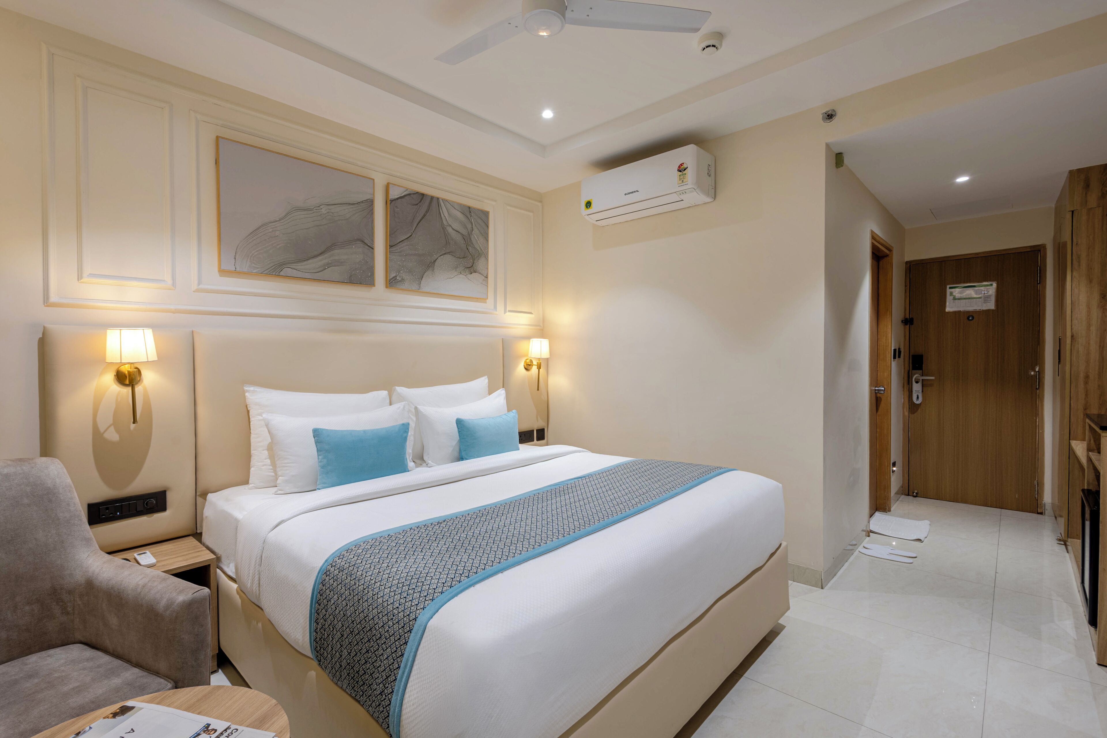 Een hotelkamer met een bed, nachtlampjes, een bureau, een stoel, een plafondventilator en een airconditioner.