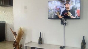Un salon moderne avec un téléviseur à écran plat fixé au mur, un meuble de rangement blanc en dessous et une table basse en bois au premier plan.