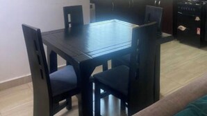 Un coin repas avec une table et des chaises, une cuisine équipée de placards et dotée d’une fenêtre, et un tableau encadré accroché au mur.