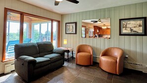 A living room with a dark green sofa, two leather armchairs, a ceiling fan, and a stone-tiled floor. - Ahrens Rd Ranch (Parksville)