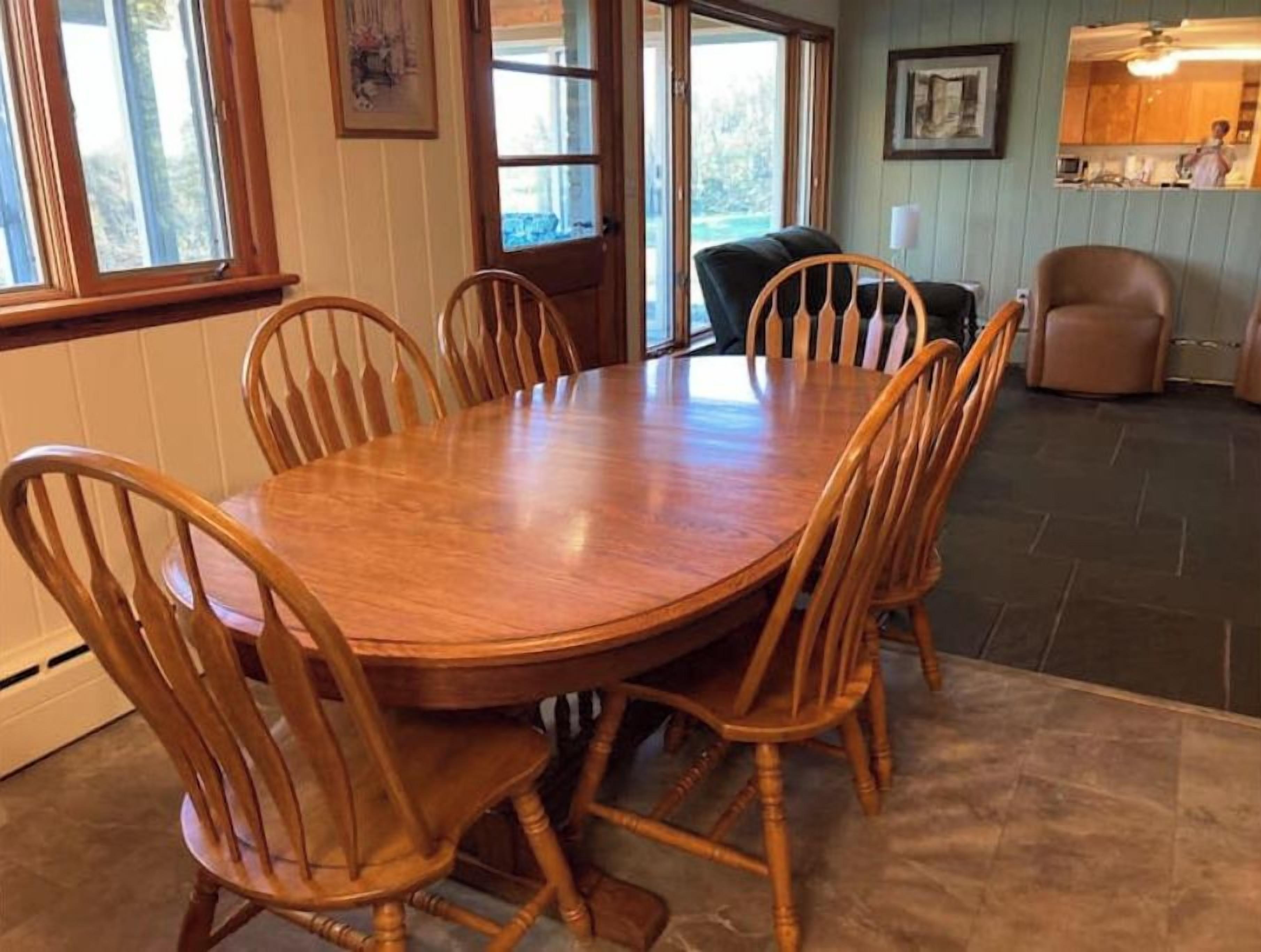 Un coin repas avec une table et des chaises en bois, une cuisine à l’arrière-plan et une vue à travers la porte vitrée.