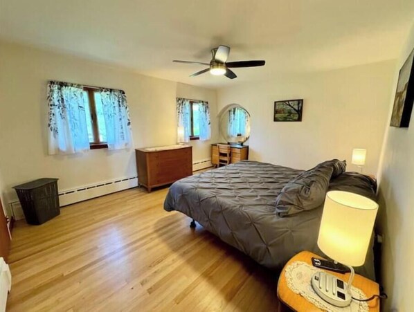A bedroom with a bed, a dresser, a vanity with a mirror, a ceiling fan, and a bedside lamp. - Ahrens Rd Ranch (Parksville)