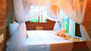 Una cama con dosel, un muro de ladrillo y una ventana que da a zonas verdes.