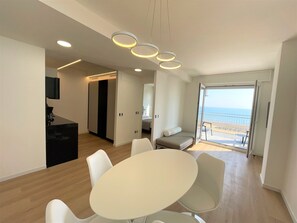 Un salón moderno con una mesa redonda y sillas, un sofá, y vista al mar a través de una puerta corrediza.