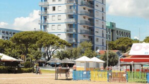 Un edificio de varios pisos con balcones, suelo arenoso y algunos árboles.