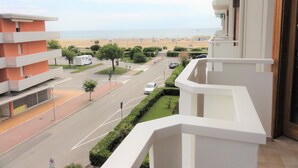 A view from a balcony overlooking a street with a beach in the background.
