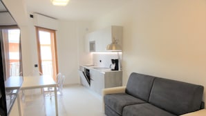 A modern kitchen with a dining area, a grey sofa, and a TV.