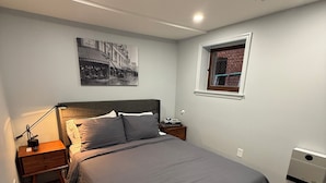 A bedroom with a large bed, a nightstand, a lamp, a heater, a window, and a wall-mounted air conditioner. - 1BR Bloomingdale Retreat with Private Entry. Walkable & Quiet Neighborhood.   (Washington)