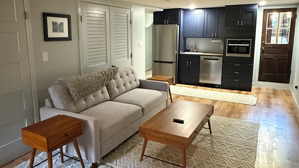 A living room with a sofa, coffee table, and a rug. There is a kitchen area with cabinets and appliances in the background. - 1BR Bloomingdale Retreat with Private Entry. Walkable & Quiet Neighborhood.   (Washington)