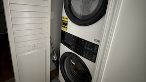 A front-loading washing machine in a laundry room with a closed door and a vacuum cleaner nearby. - 1BR Bloomingdale Retreat with Private Entry. Walkable & Quiet Neighborhood.   (Washington)