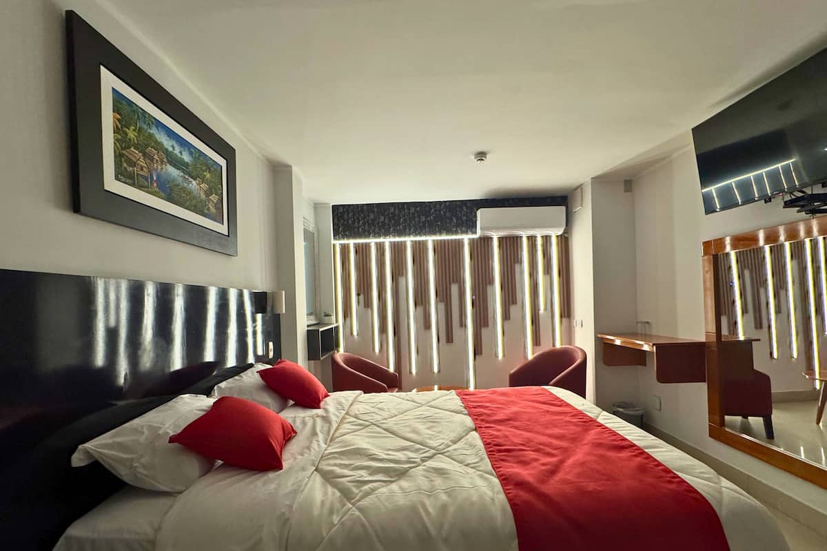 Une chambre d’hôtel avec un grand lit, un bureau, une chaise, une télévision et une fenêtre avec des rideaux.