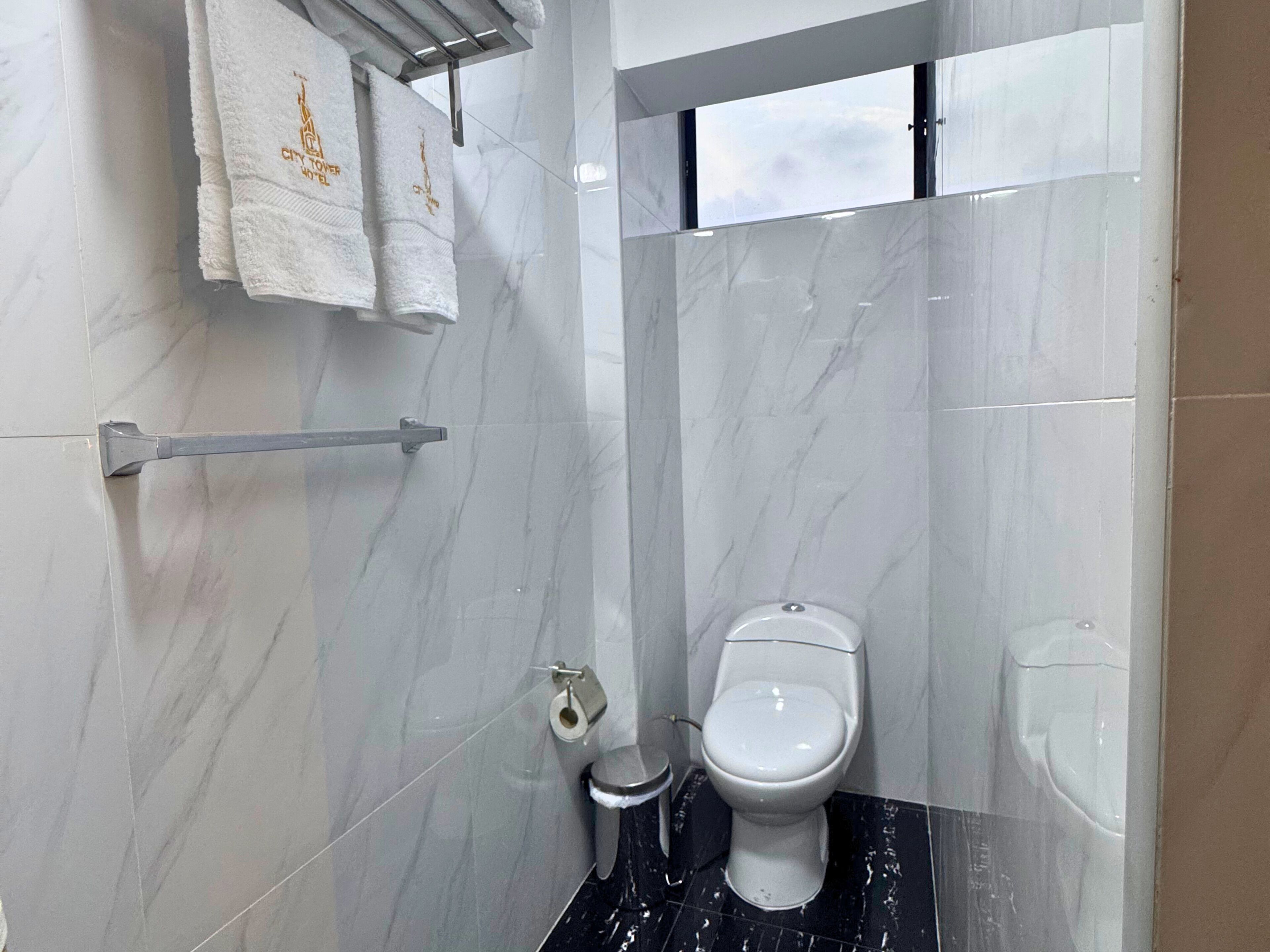 A modern bathroom with a toilet, a hand dryer, and a towel rack with towels.