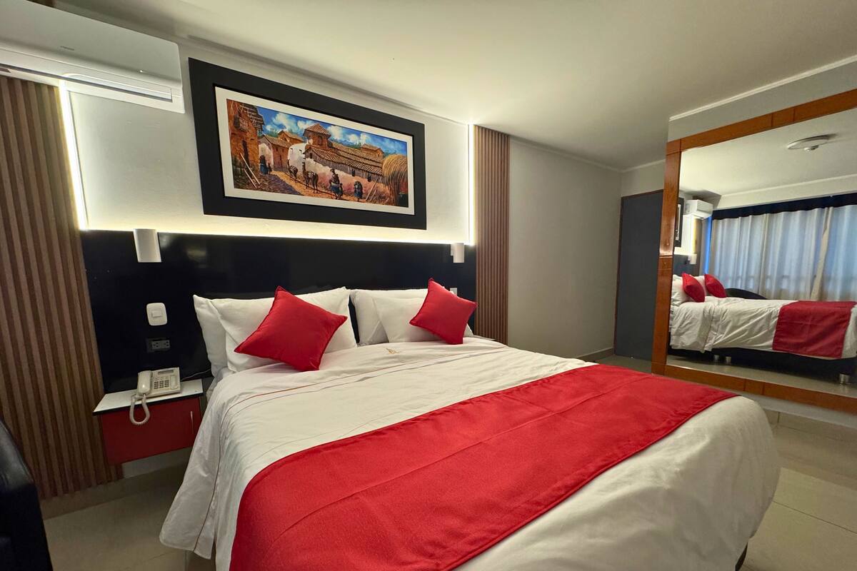 Une chambre d’hôtel avec un grand lit, un téléphone sur la table de chevet, un tableau au-dessus du lit et un miroir au mur.