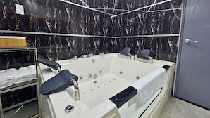A modern bathroom with a large bathtub, marble walls, and a glass-enclosed shower area. - City Tower Hotel (Santiago de Surco)