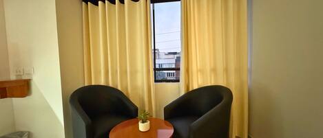 A room with two black armchairs, a small wooden table, and a potted plant.