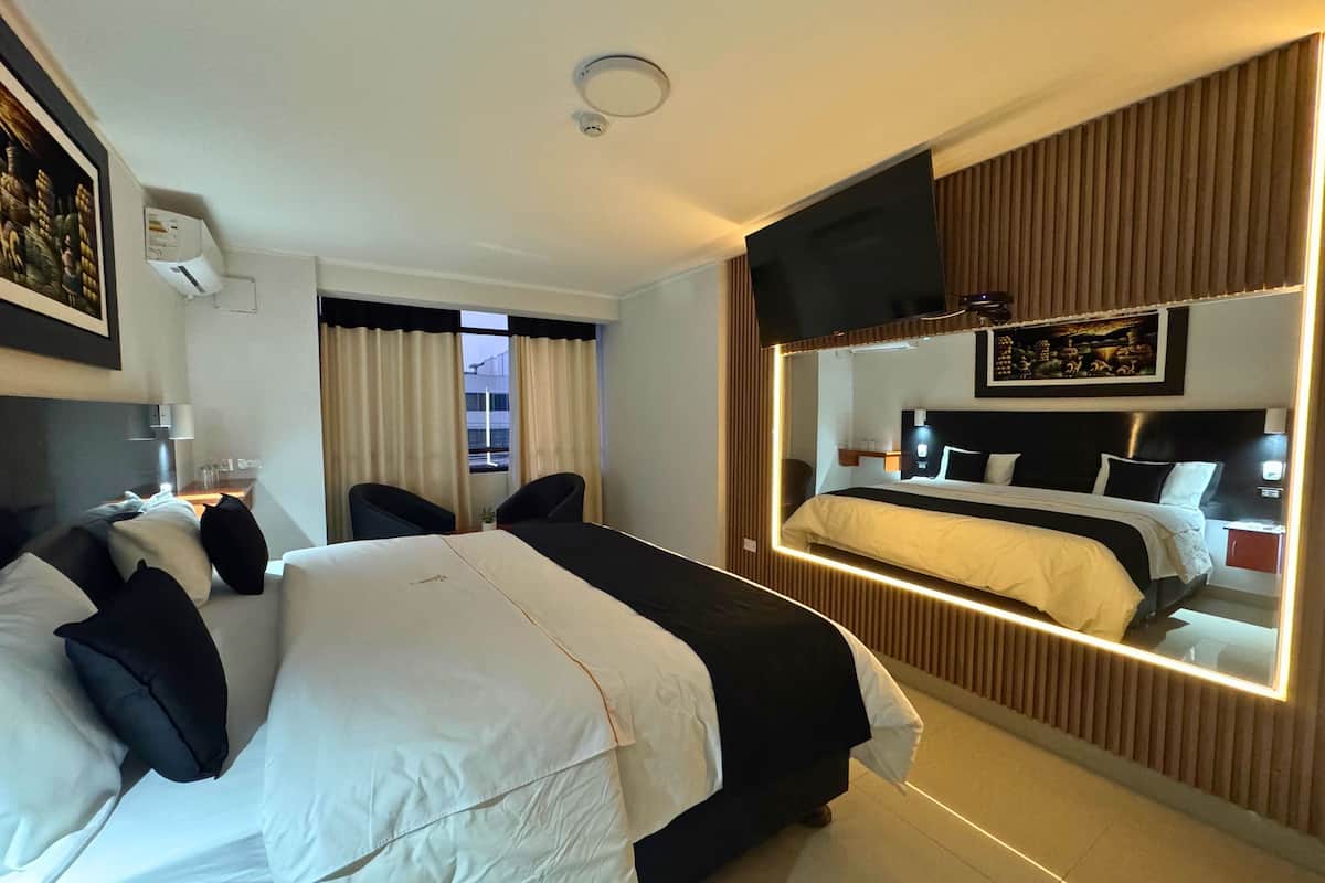 Une chambre d’hôtel avec un grand lit, un téléviseur fixé au mur, une fenêtre avec des rideaux et un luminaire au plafond.